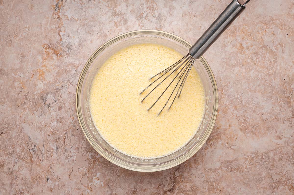whisking wet ingredients for pancakes in a glass mixing bowl.