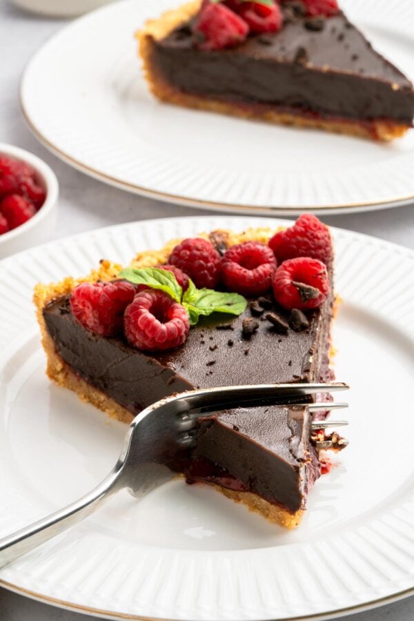 fork cutting into a slice of chocolate raspberry tart.