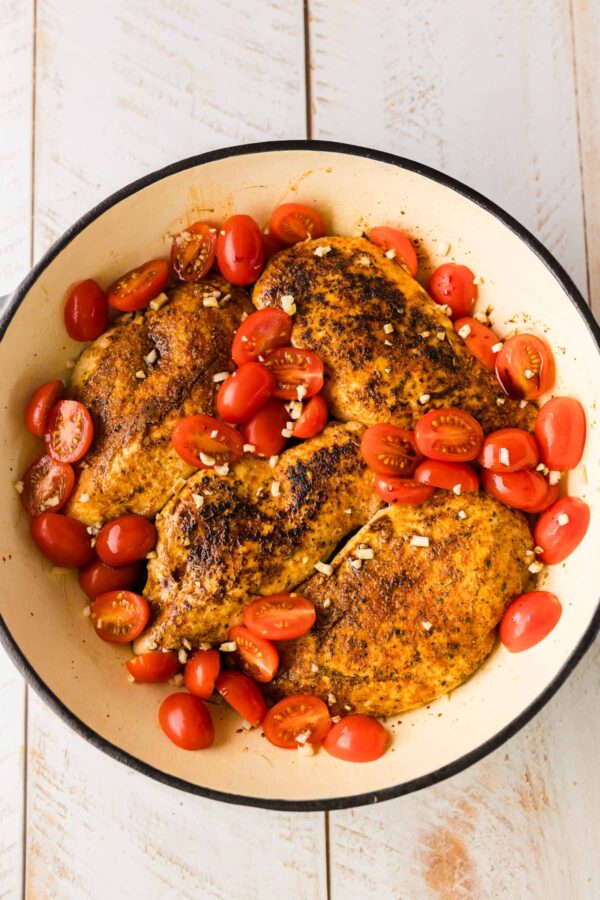 adding tomatoes and garlic to seared chicken breasts.