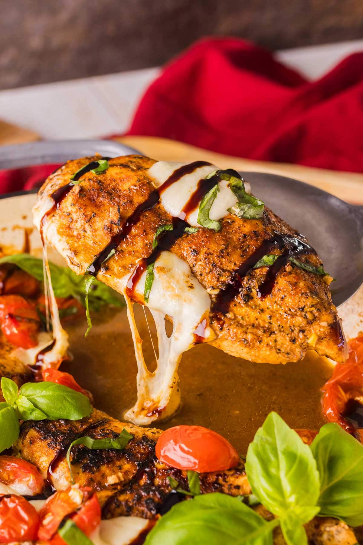 serving one piece of caprese chicken from a large pan.