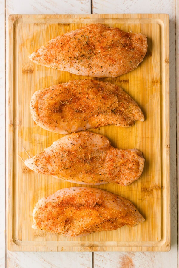 well seasoned uncooked chicken breasts on a cutting board.