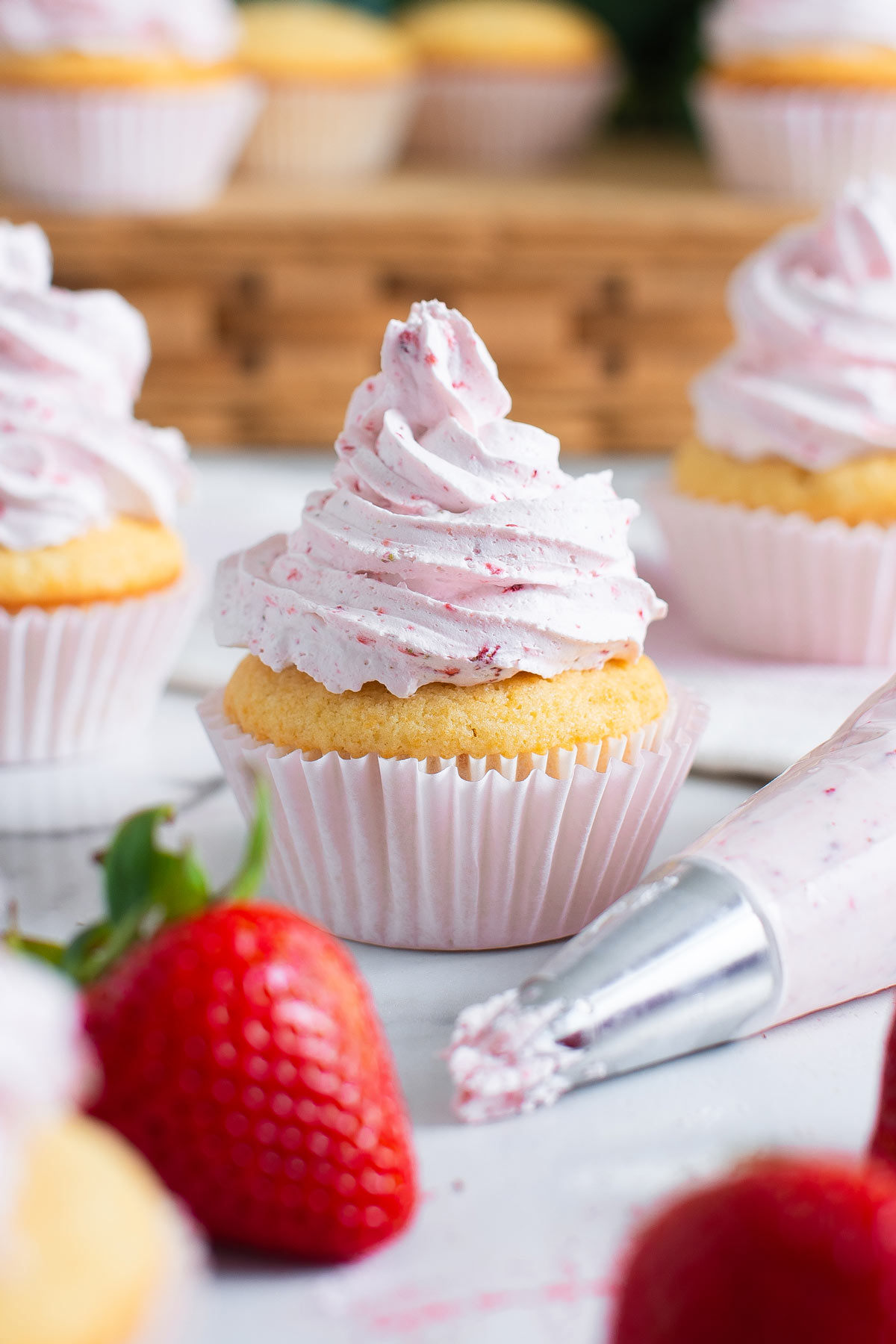 piping a tall swirl of strawberry frosting onto a cupcake.