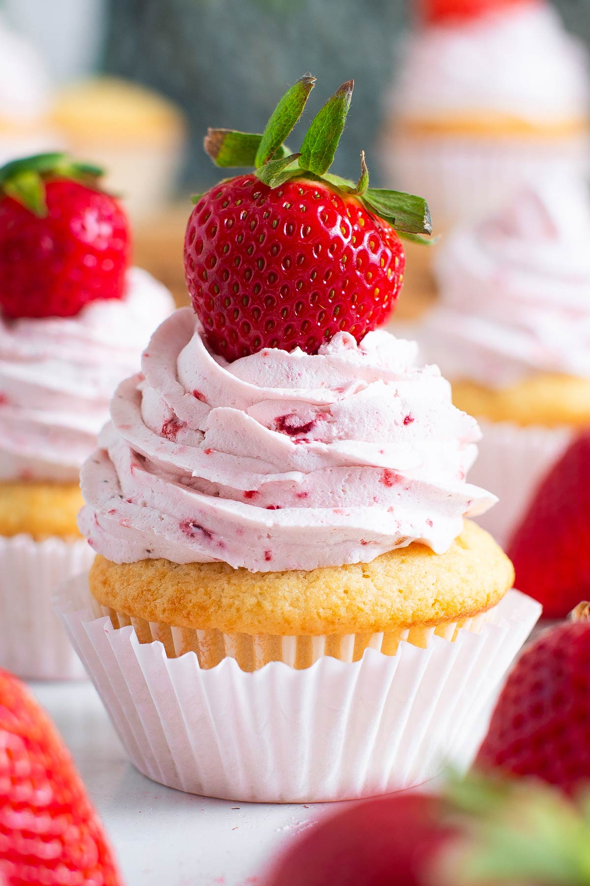 vanilla cupcakes with a giant swirl of strawberry frosting and a fresh strawberry.
