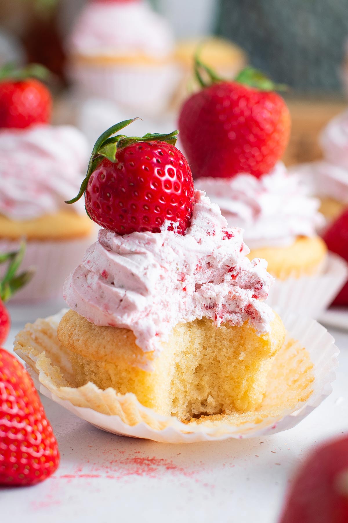 fluffy strawberry and cream cupcake with a large bite taken out of the cupcake.