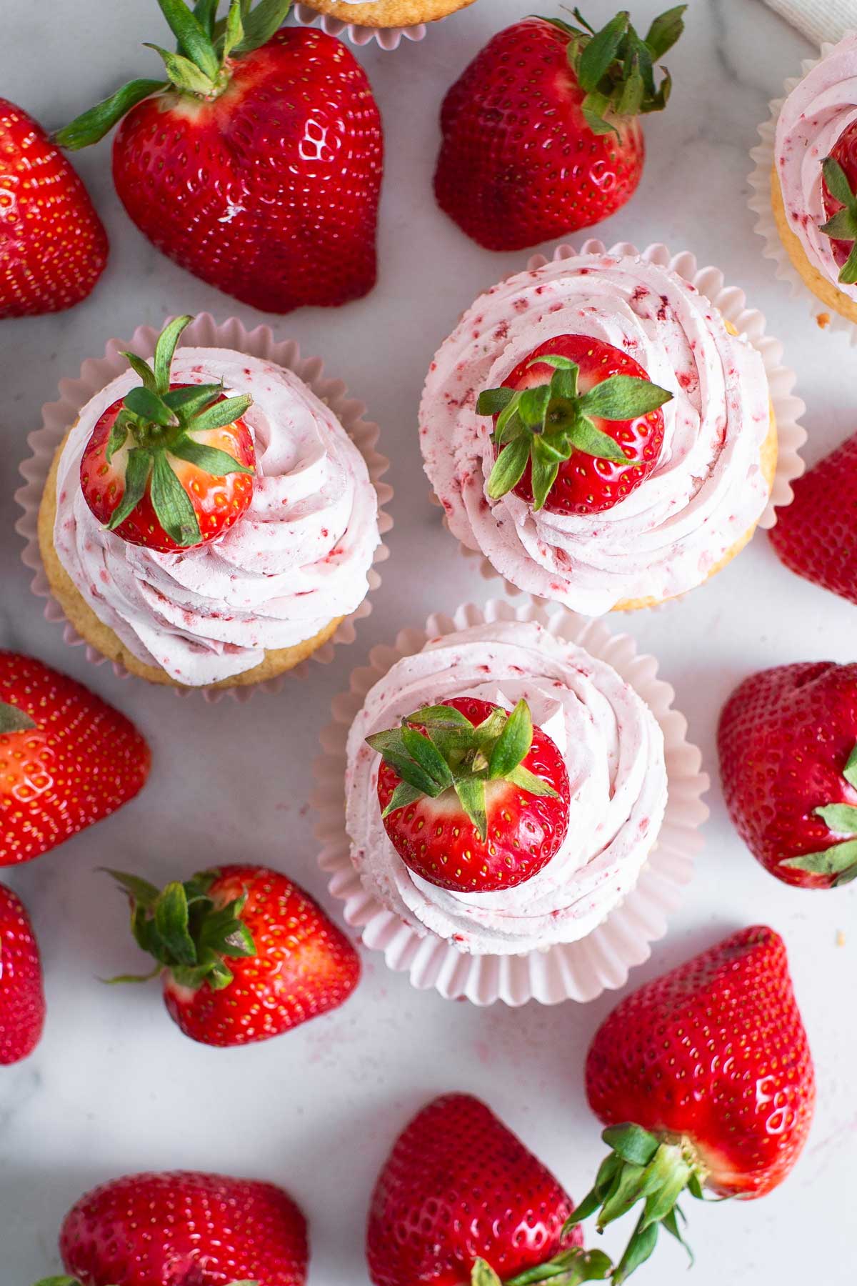 overhead view of generous swirls of strawberry frosting on cupcakes.