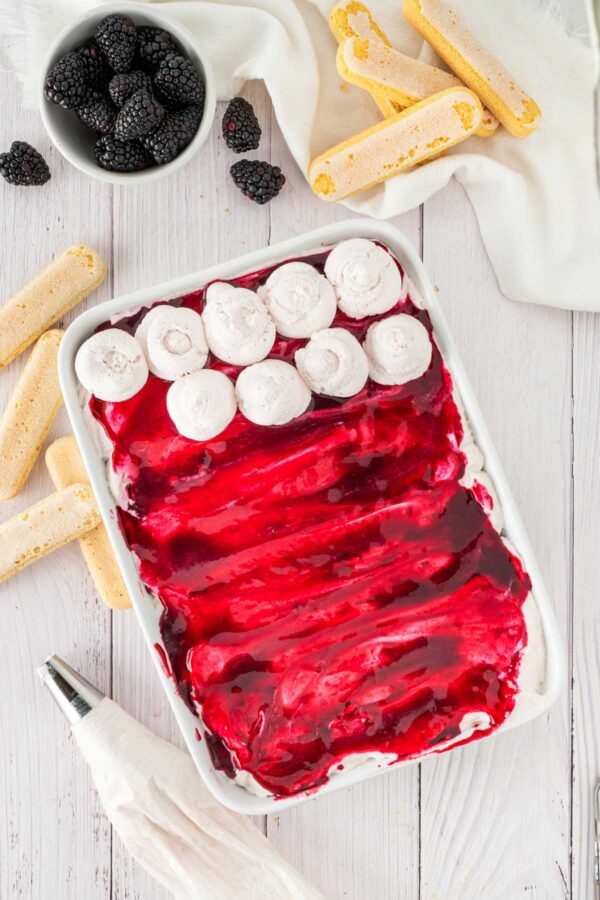 piping blackberry whipped cream on top of layers of blackberry tiramisu.