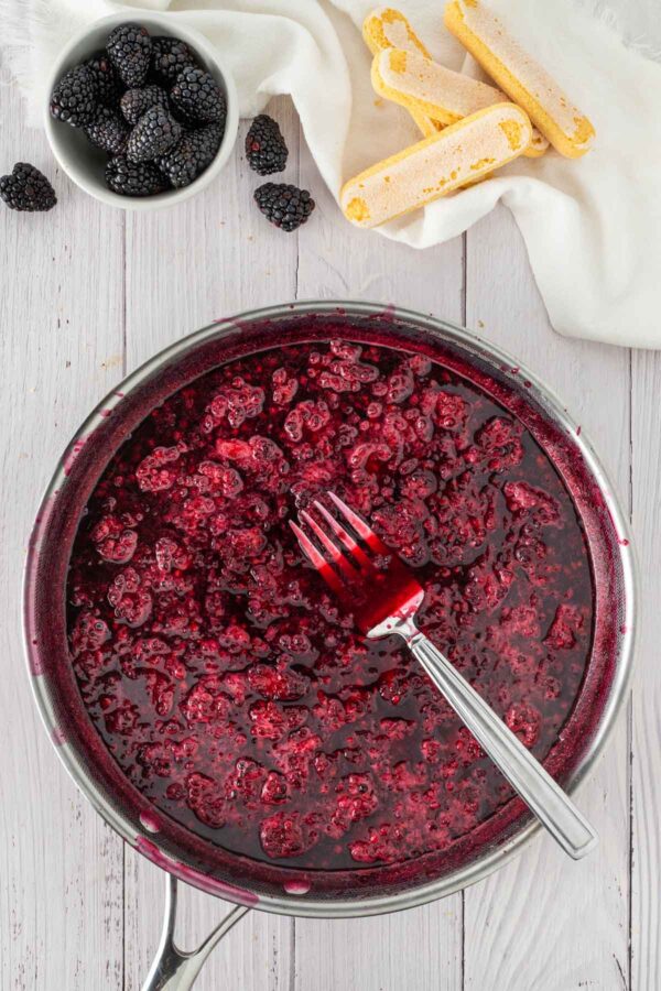 mashing cooked blackberries to make blackberry syrup.