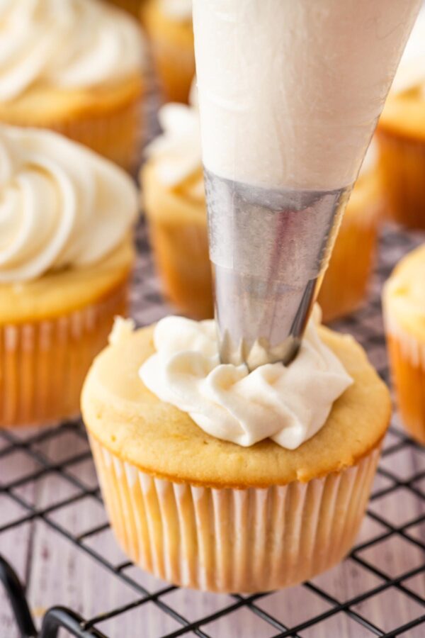 piping cream cheese frosting onto cupcakes.