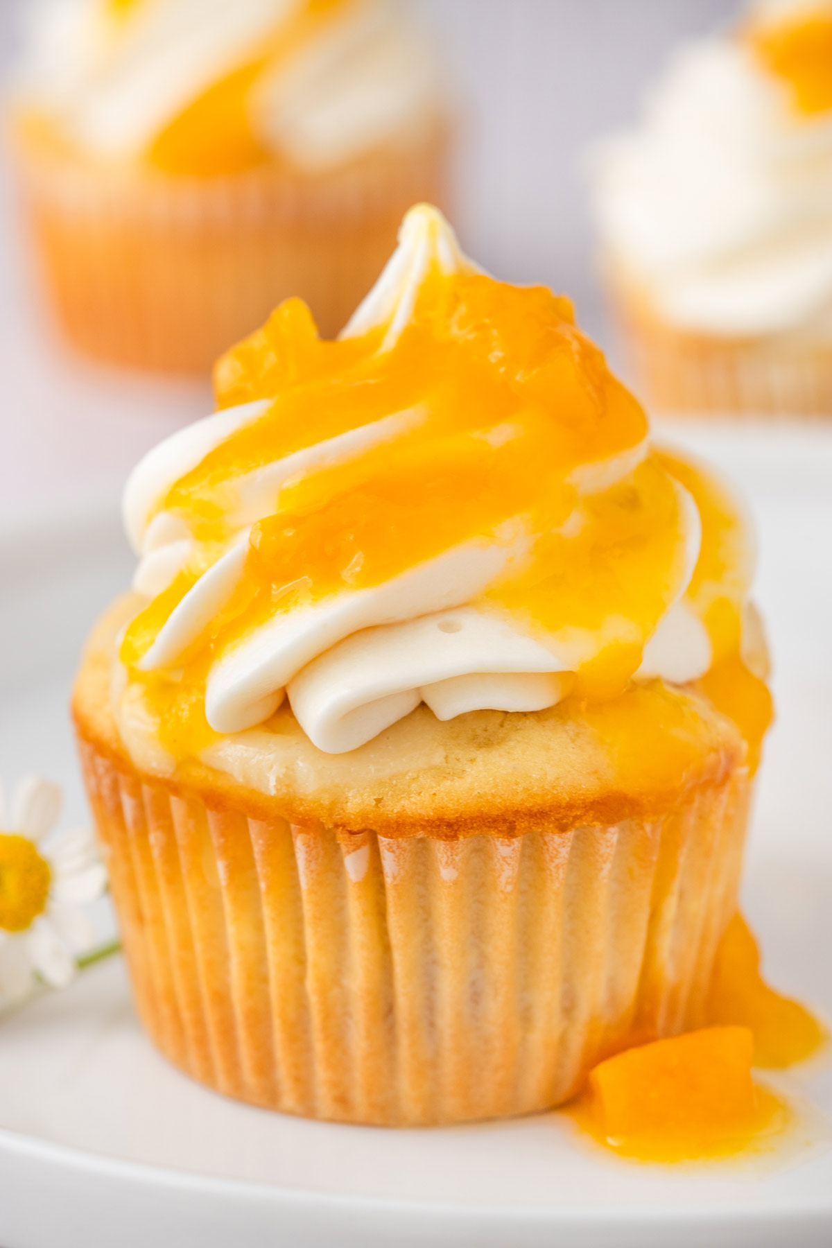 peach cupcake with a tall swirl of frosting and peach glaze dripping down the sides.