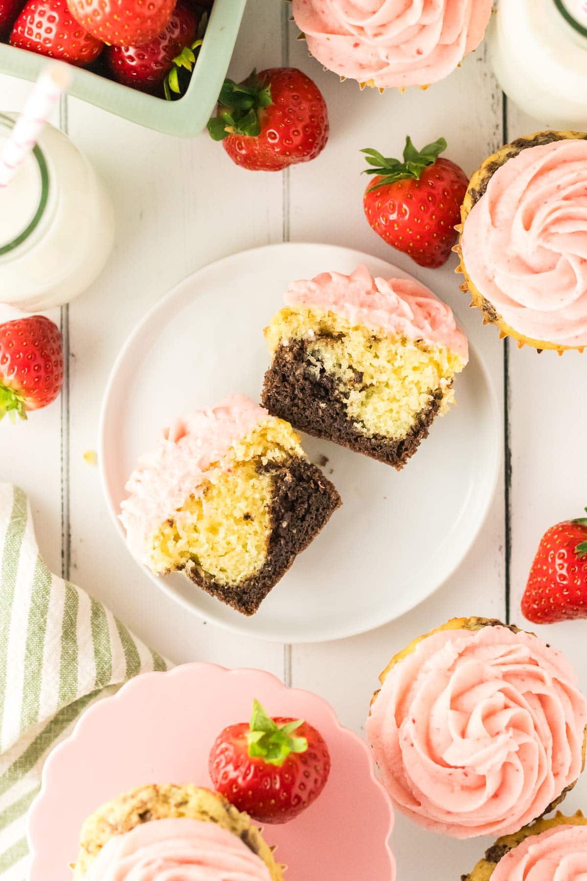 neapolitan cupcake cut in half to highlight the chocolate and vanilla cake layers and strawberry frosting.