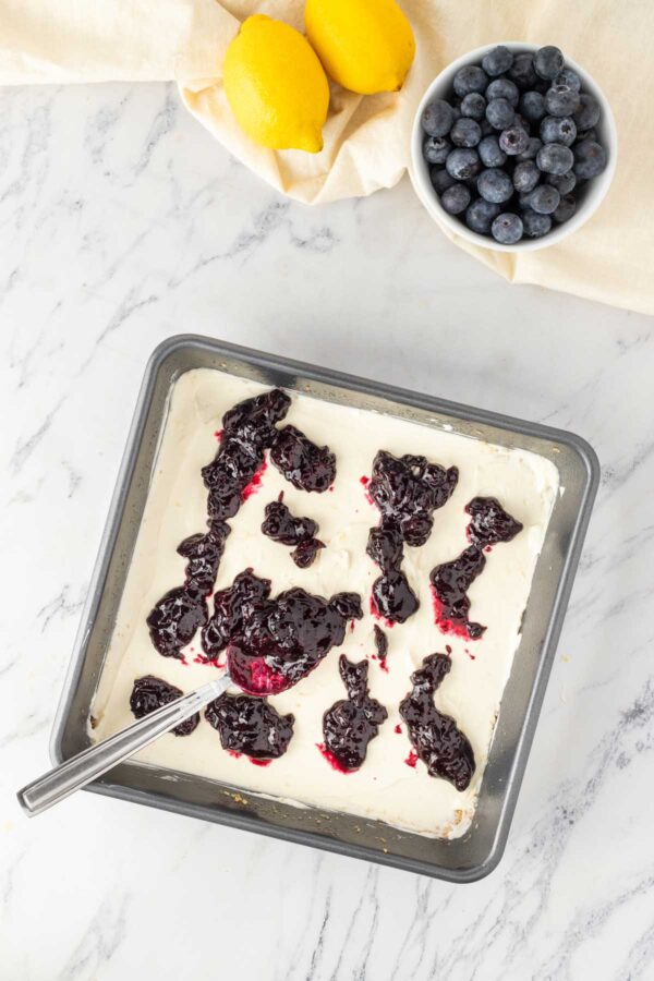 adding cooked blueberry jam to a layer of no bake cheesecake.