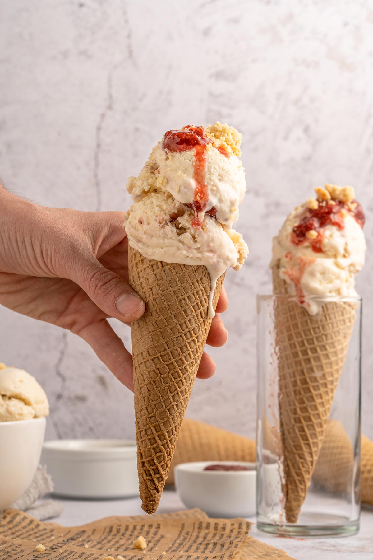 two scoops of strawberry shortcake ice cream in a tall ice cream cone.