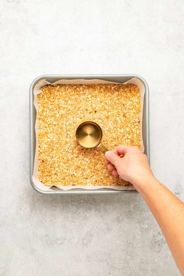 pressing an oatmeal coconut crust into a baking pan.