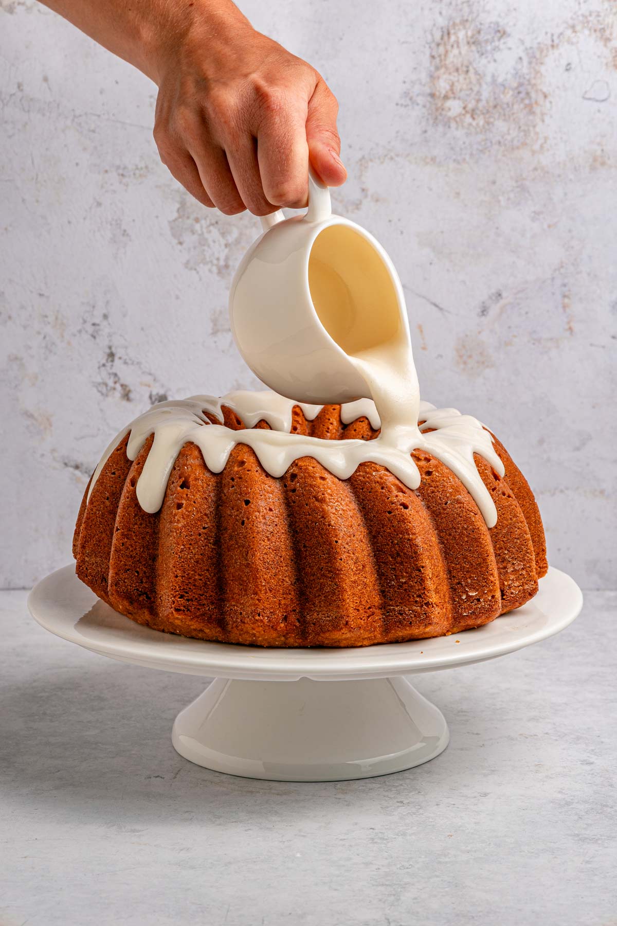pouring a thick vanilla glaze on top of a pistachio bundt cake.