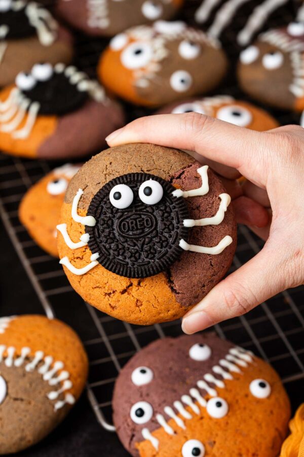 large cookie decorated with an oreo spider held in a hand.
