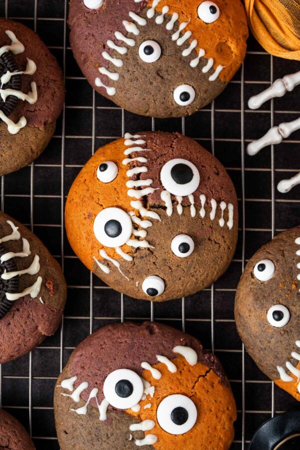 Halloween cookies decorated to look like monsters with candy eyeballs and white chocolate stitches.