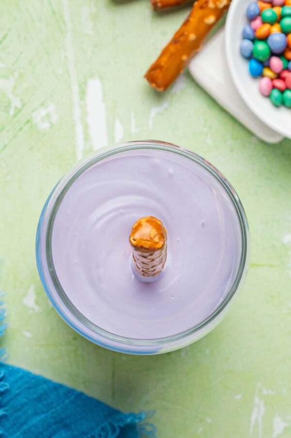 dipping a pretzel rod into melted candy bark.