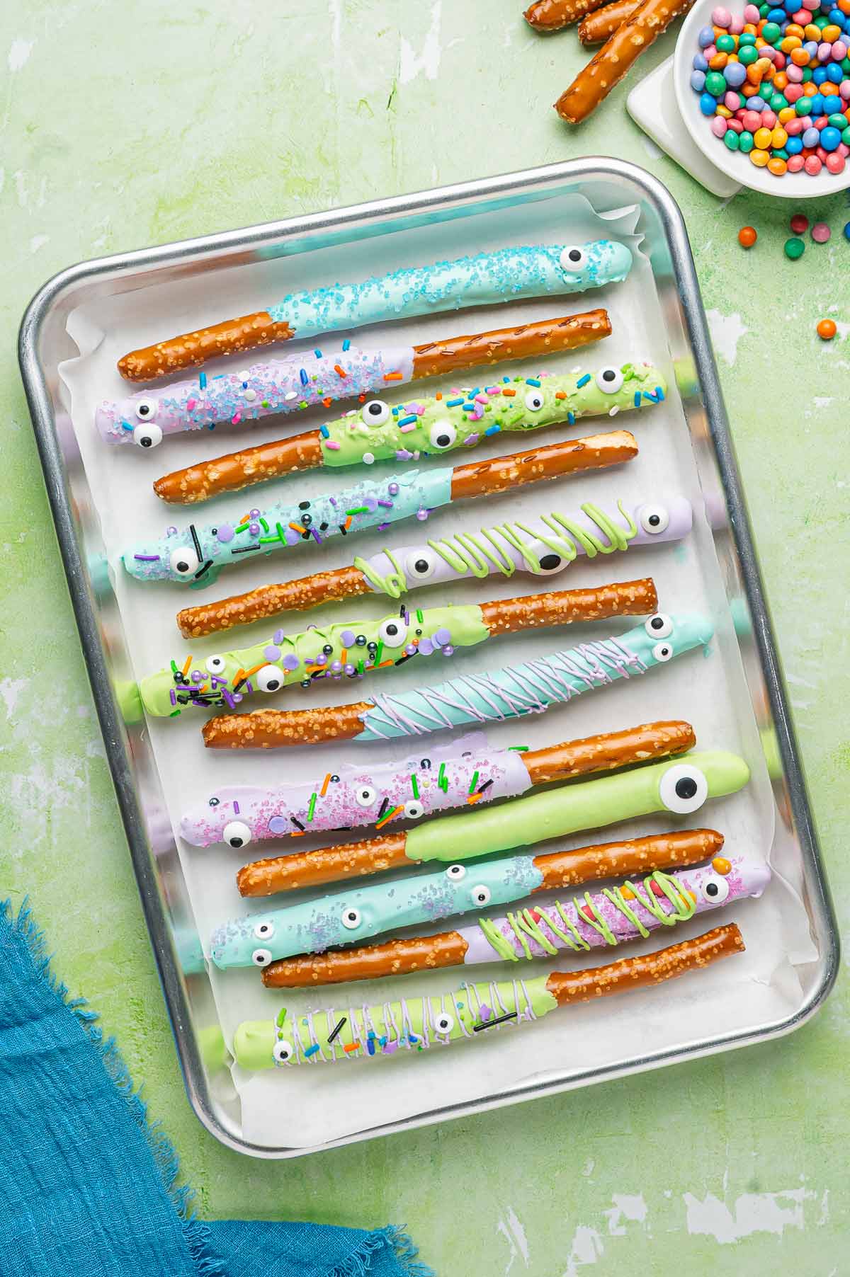 decorated halloween pretzel rods lined up on a sheet pan lined with parchment paper.