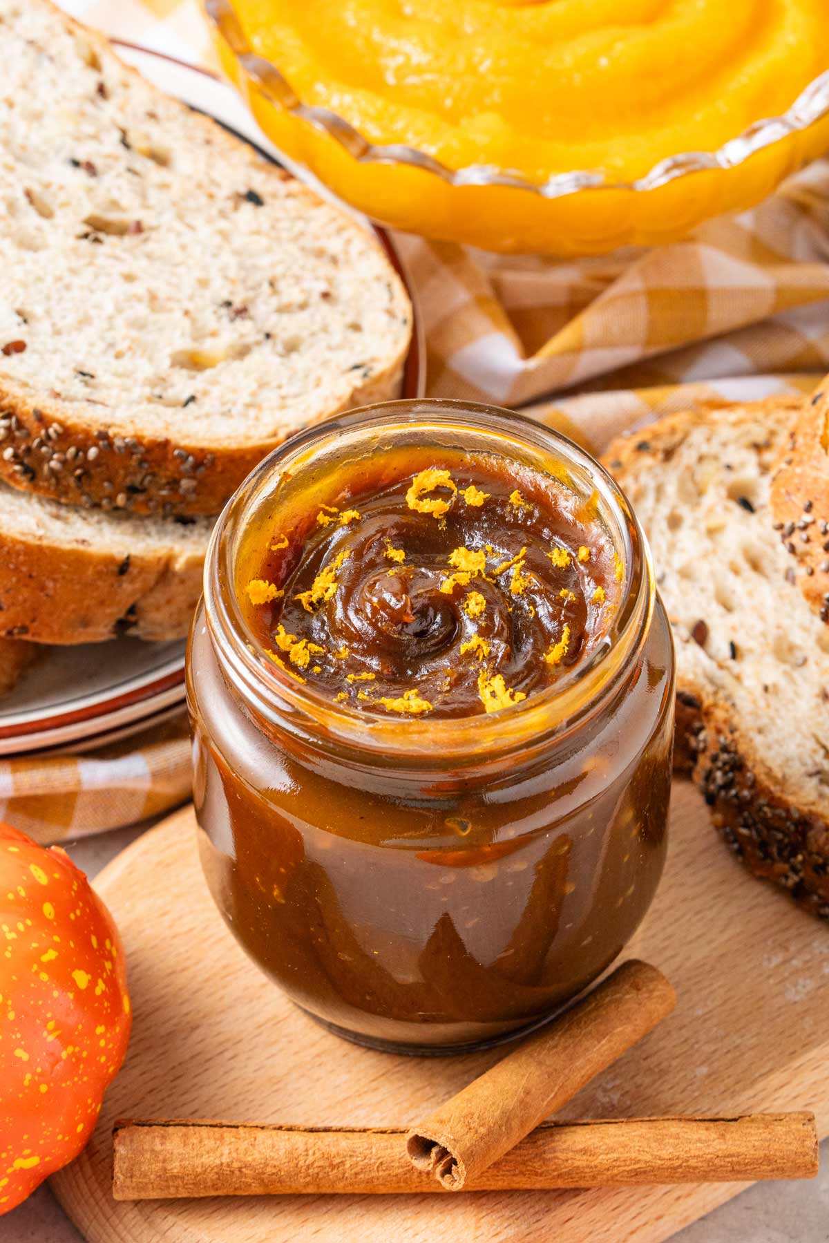 jar of homemade pumpkin butter surrounded by cinnamon sticks and slices of bread.
