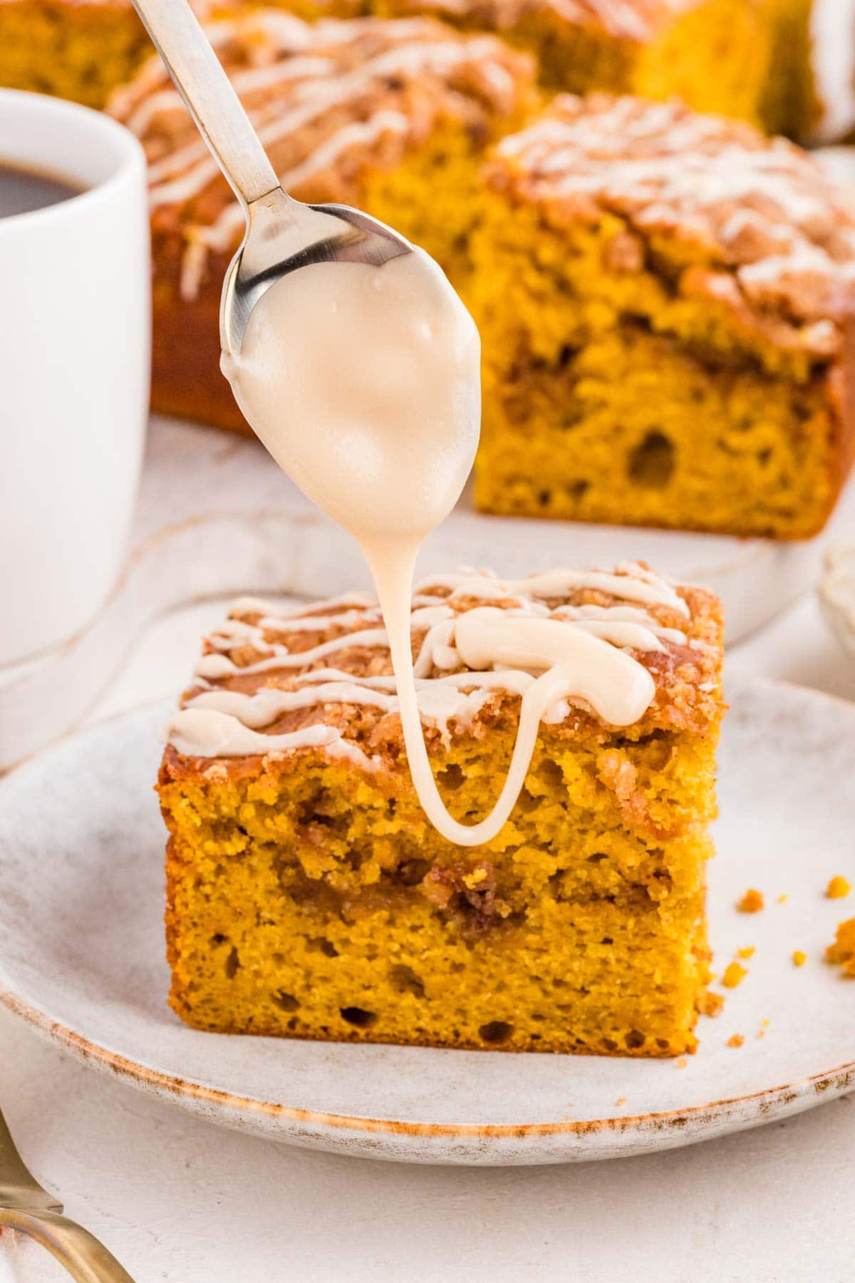 drizzling maple glaze over a slice of pumpkin coffee cake.